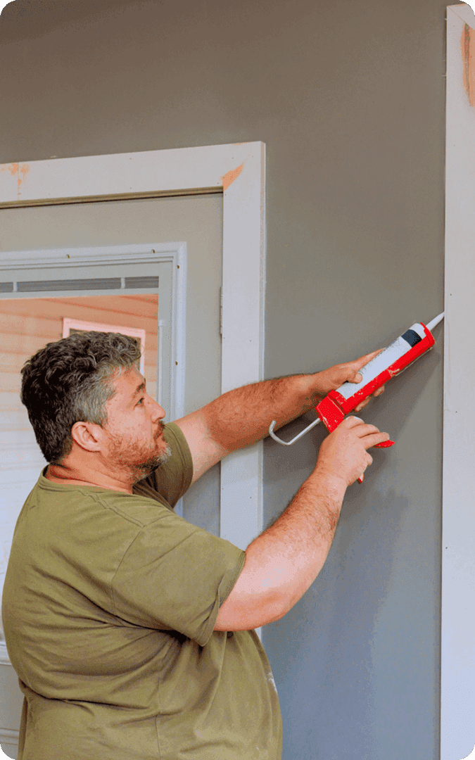 Man using caulking gun on wall.