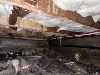 Crawl space with insulation and exposed pipes.