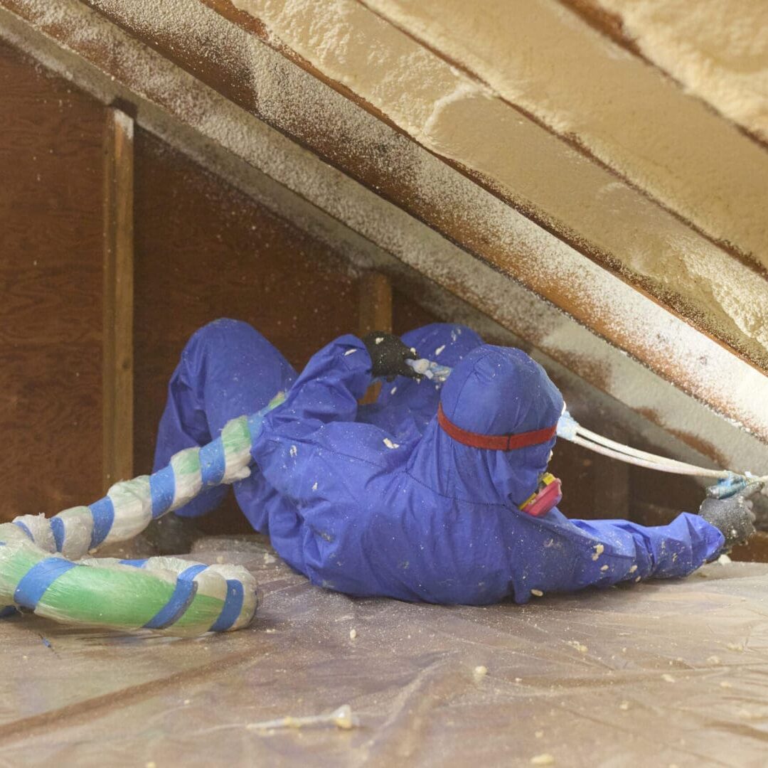 Worker applying spray foam insulation in attic.